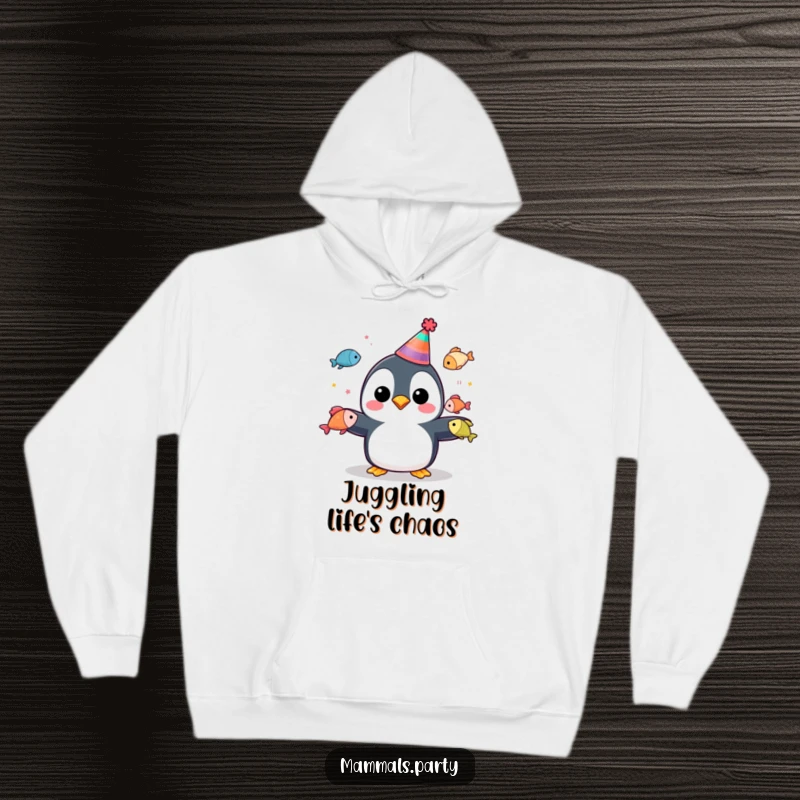 Funny penguin in a party hat juggling colorful fish, featured on a cozy hoodie for warm, festive comfort.