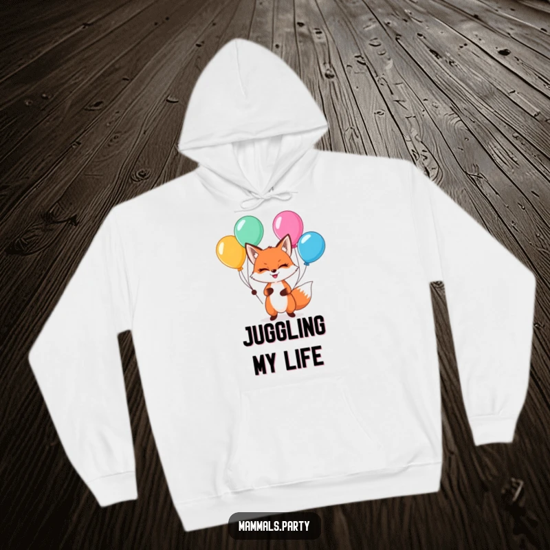 Funny kawaii fox with a sly grin, juggling balloons, on a cozy hoodie, bringing playful woodland vibes.